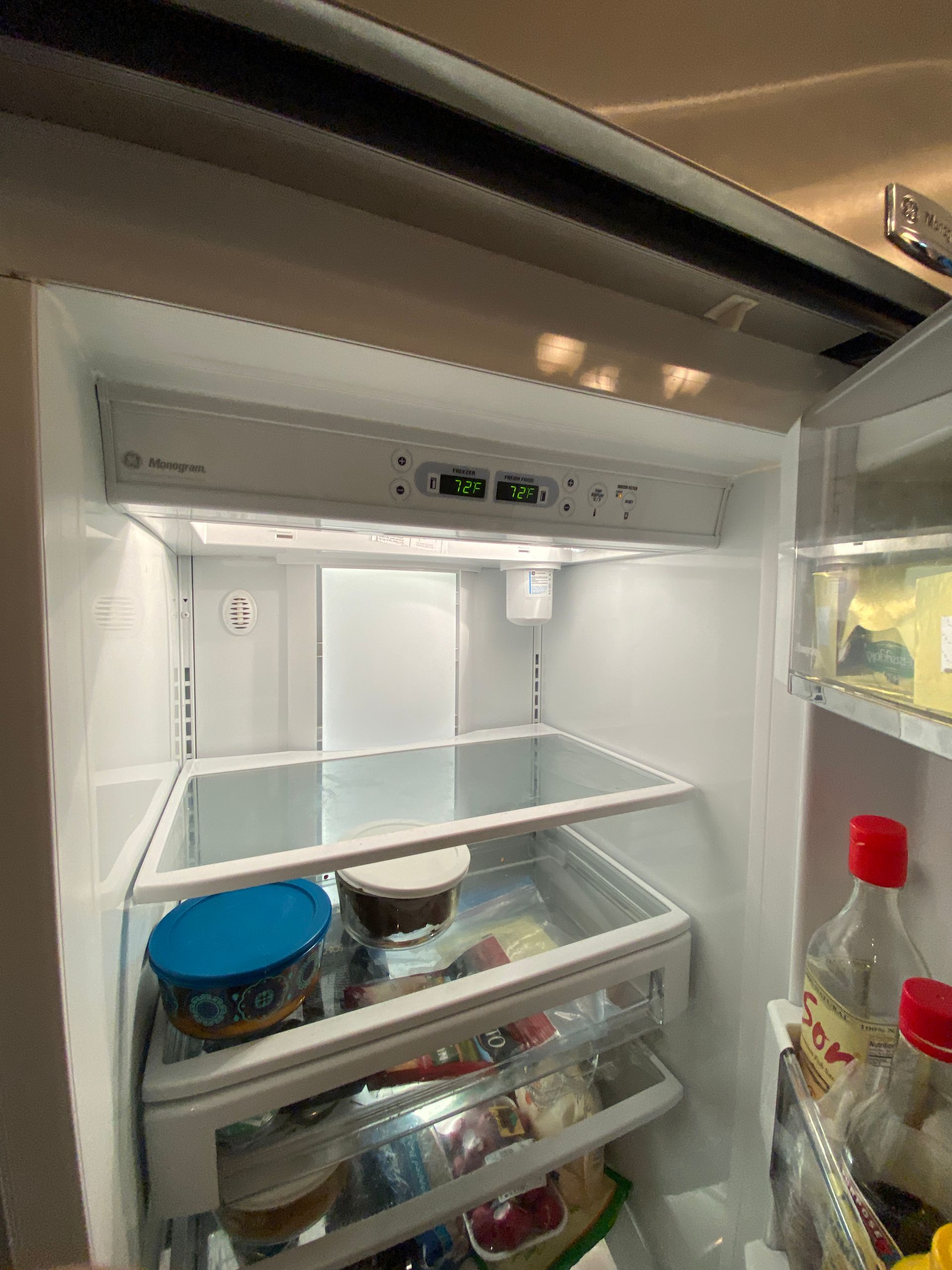 An open refrigerator interior with shelves, controls, and some food items. White interior.