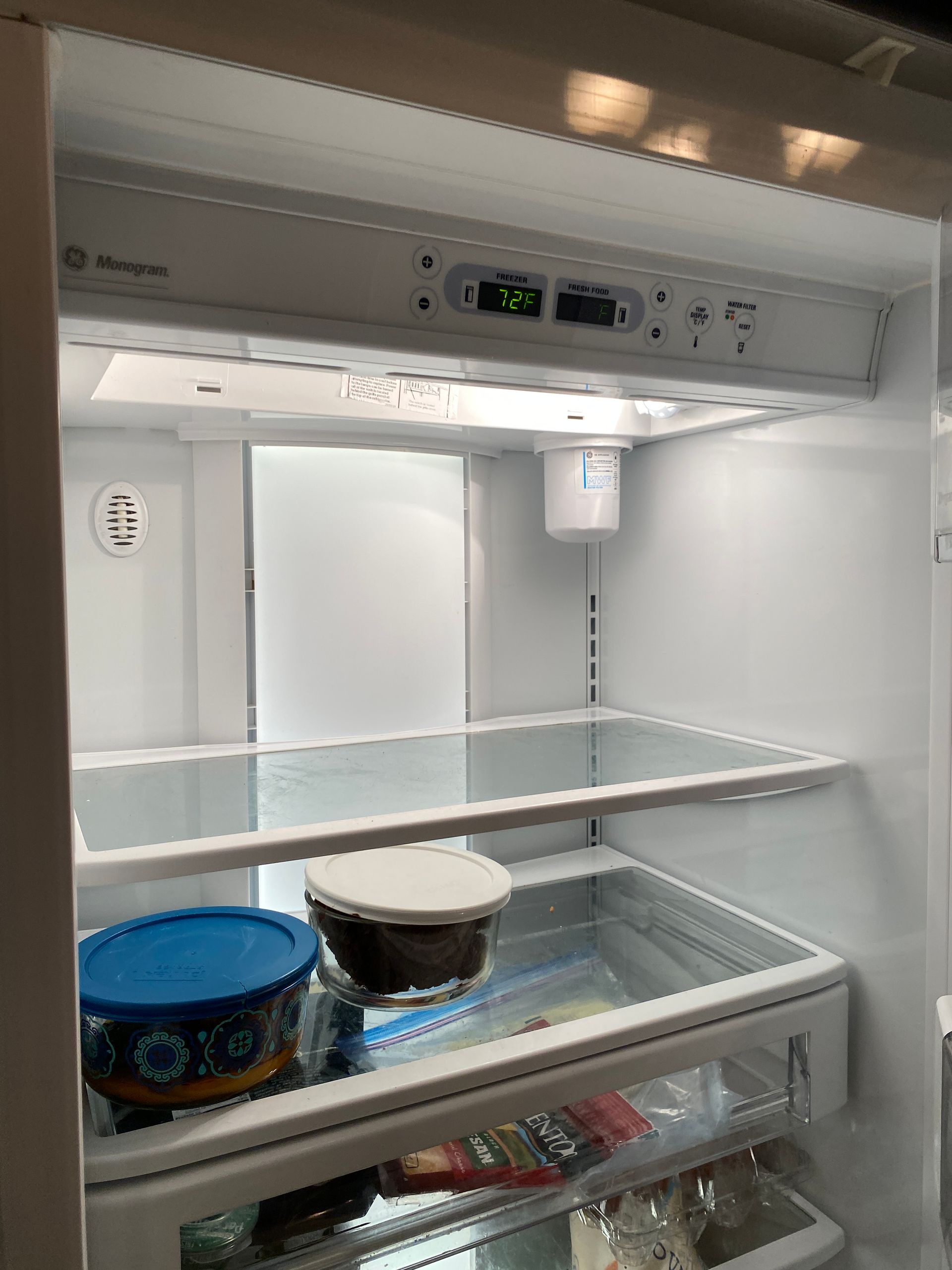 Empty refrigerator interior; two containers on bottom shelf, control panel at top. White, clean.