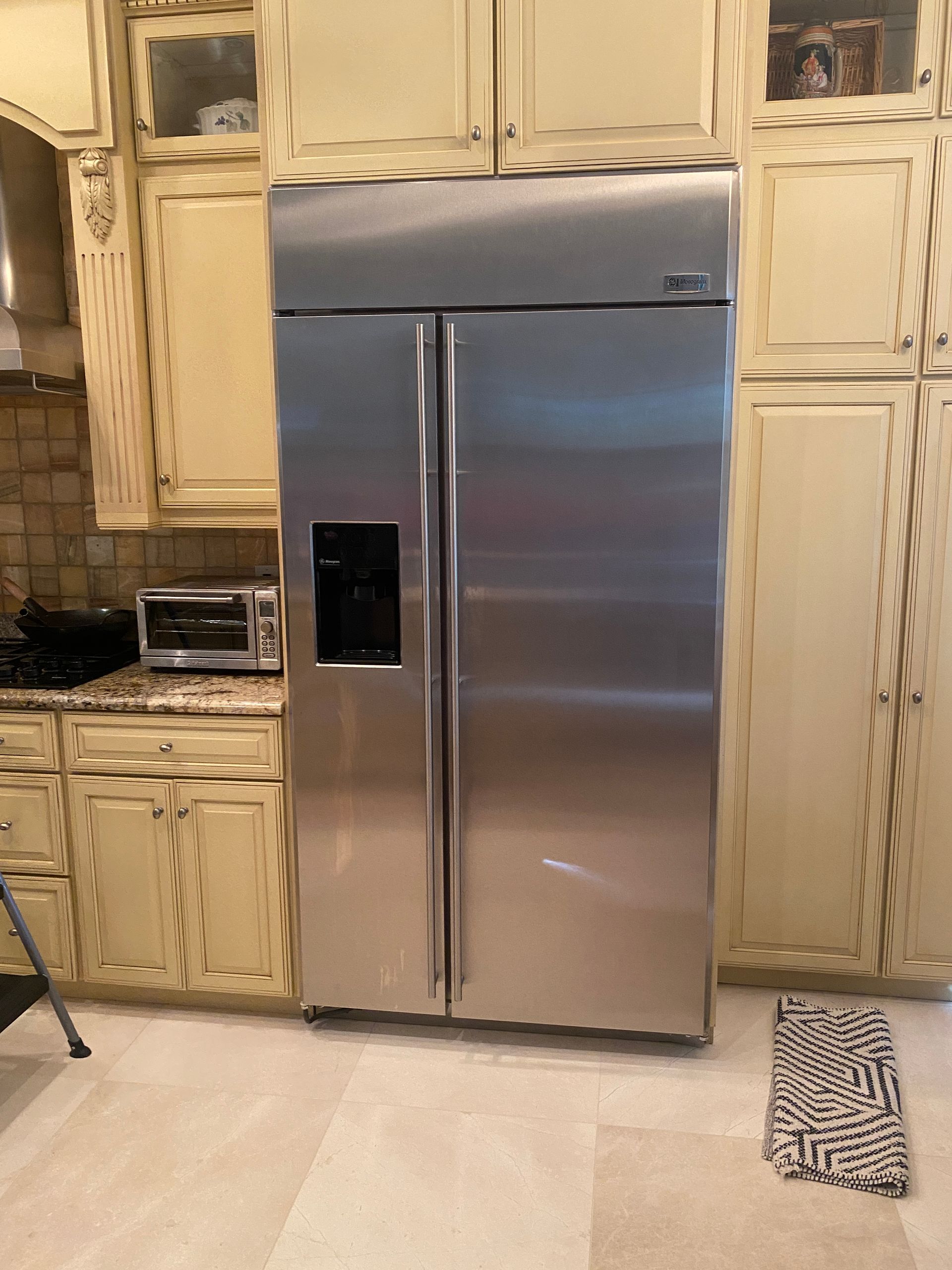 Stainless steel side-by-side refrigerator in a kitchen with cream-colored cabinets and a granite countertop.