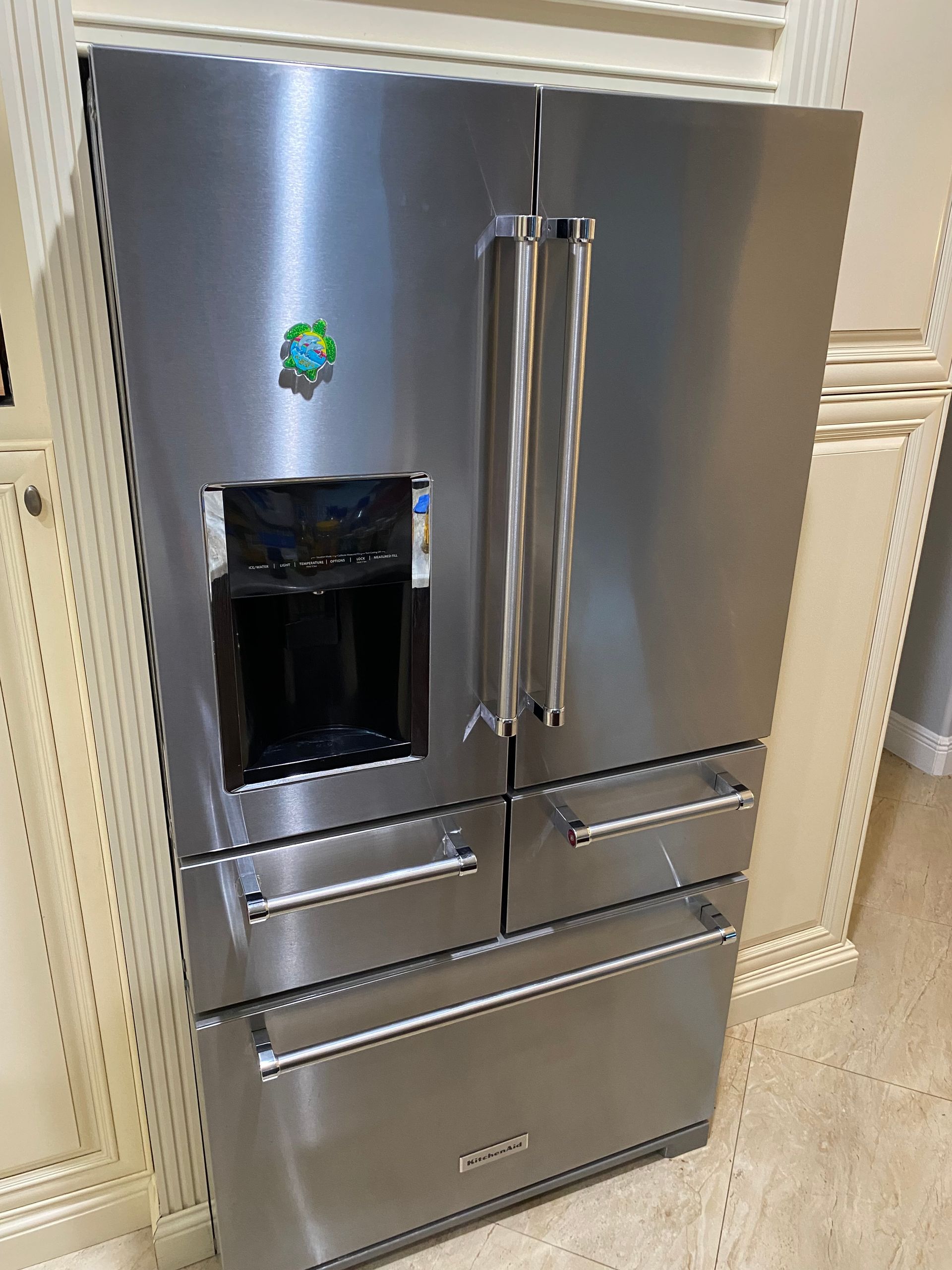Stainless steel refrigerator with four doors, water dispenser, and silver handles, built into a light-colored kitchen.