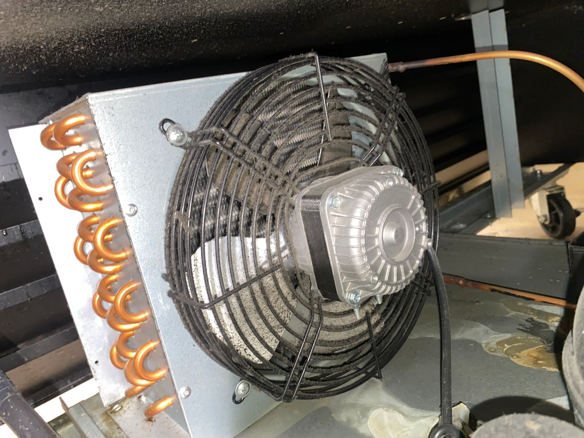 Close-up of a refrigeration unit's fan and copper coils, located in a mechanical setting.