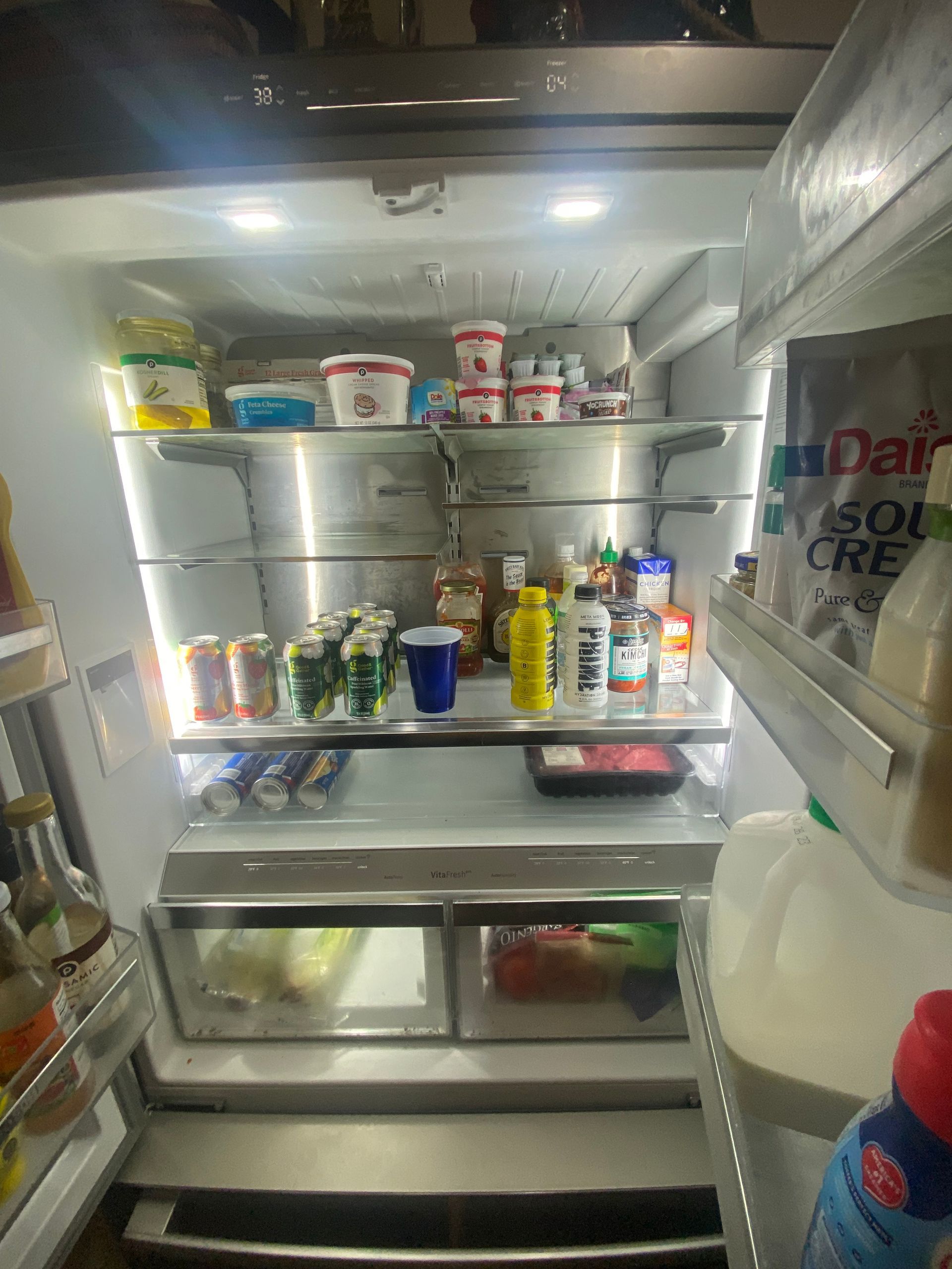 Open refrigerator filled with food and beverages. Stainless steel interior.
