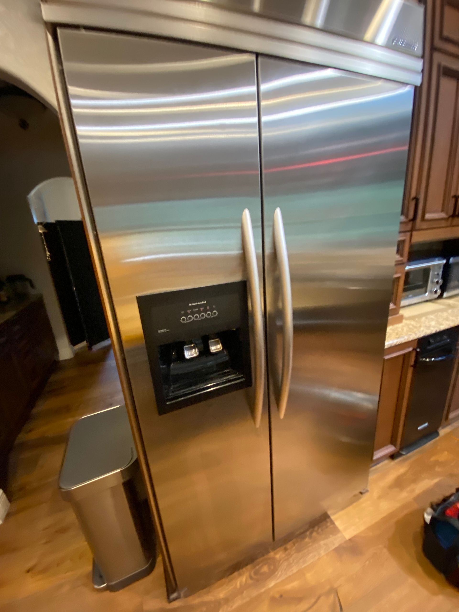 Stainless steel side-by-side refrigerator in a kitchen with wooden cabinets and floors. Features water and ice dispenser.