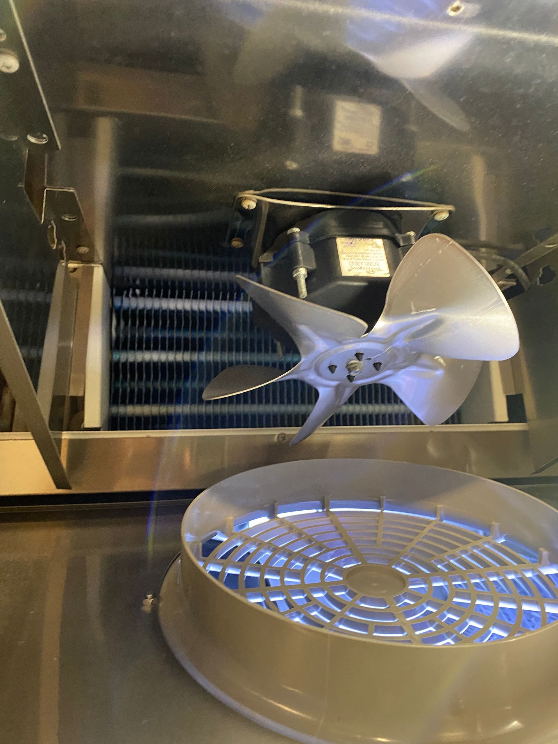 Inside a refrigerator: metal fan, cooling coils, and a light in a metal casing.