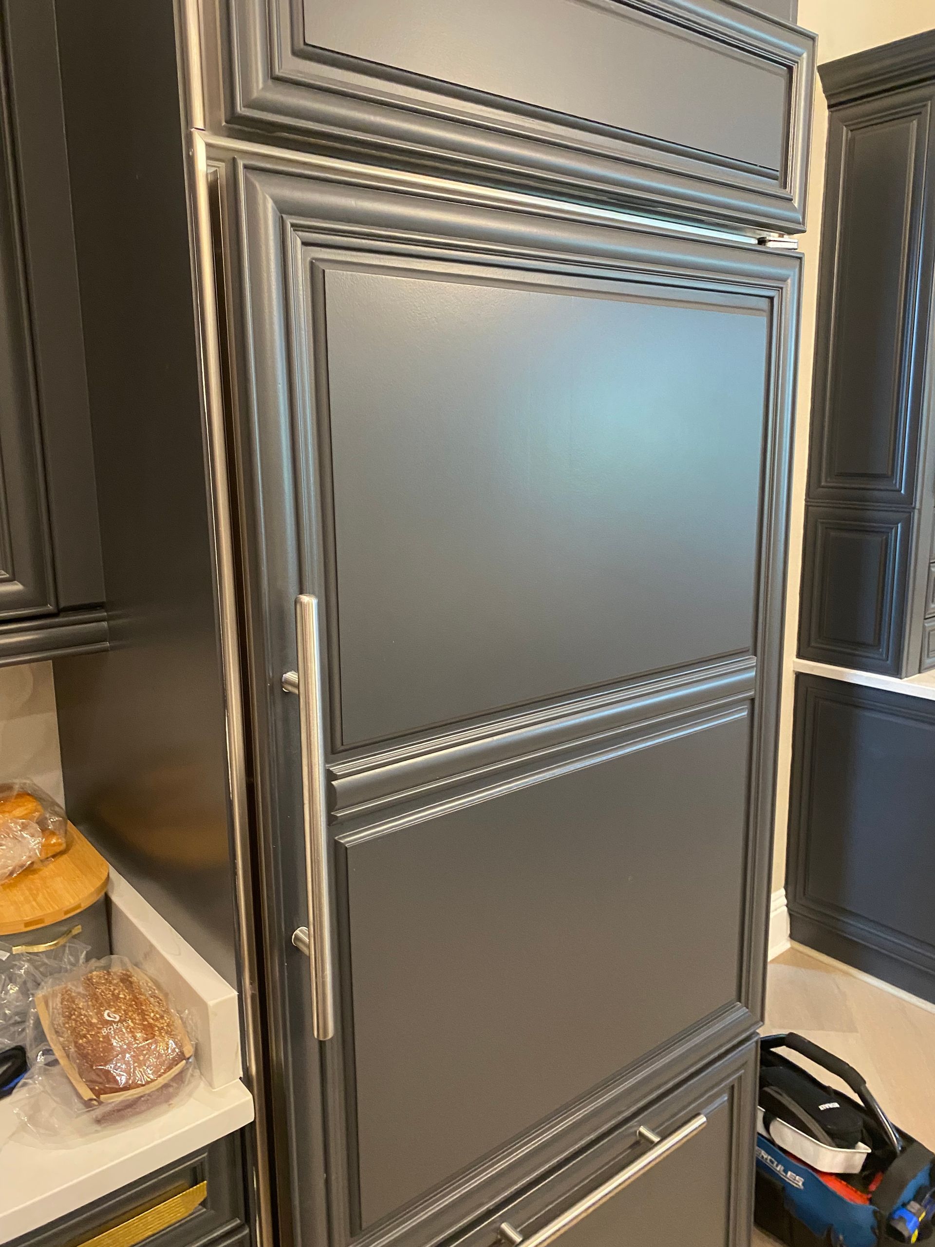 Dark gray refrigerator built into kitchen cabinetry with a stainless steel handle.