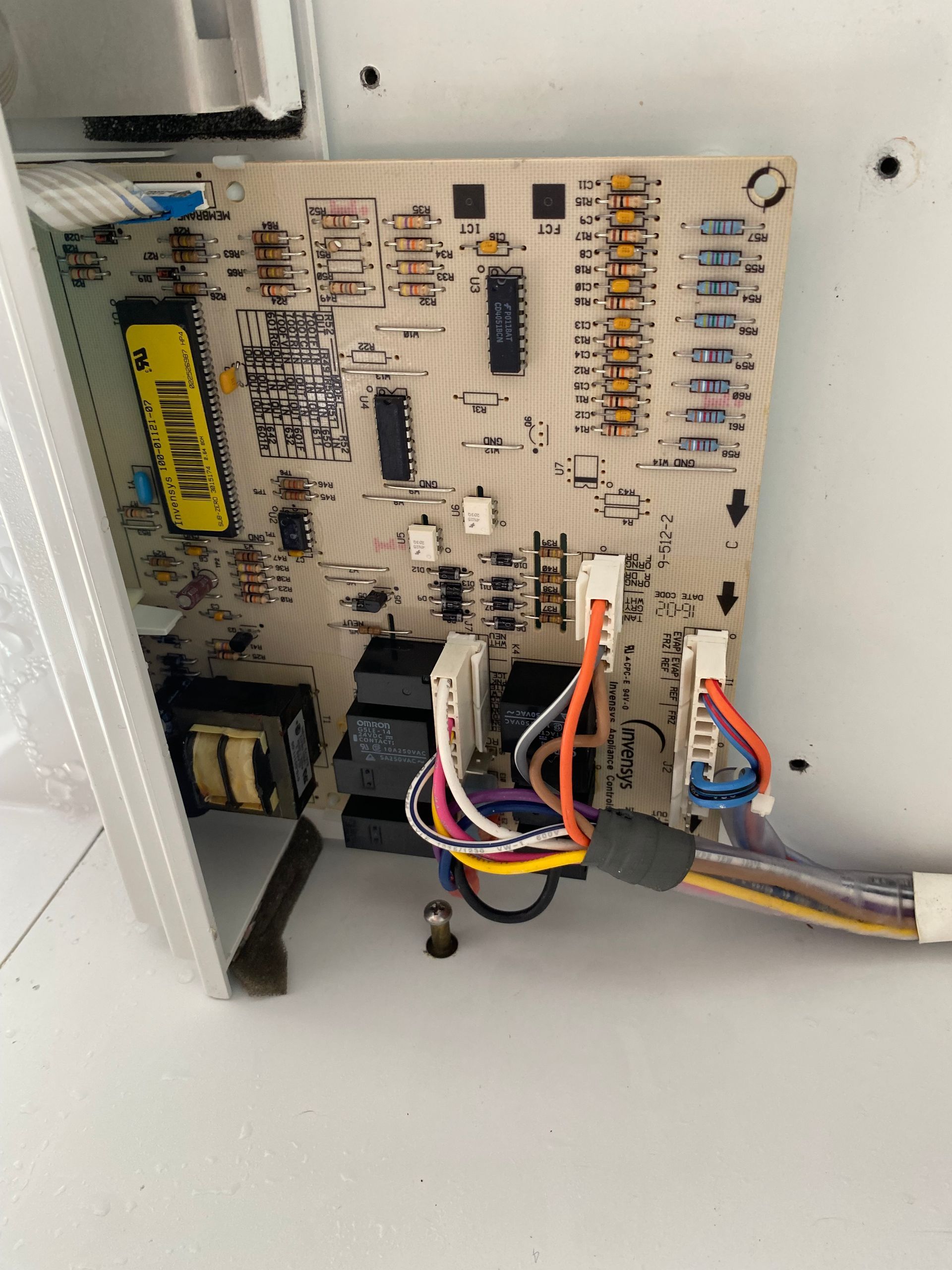 Printed circuit board with wiring and components inside a white appliance.