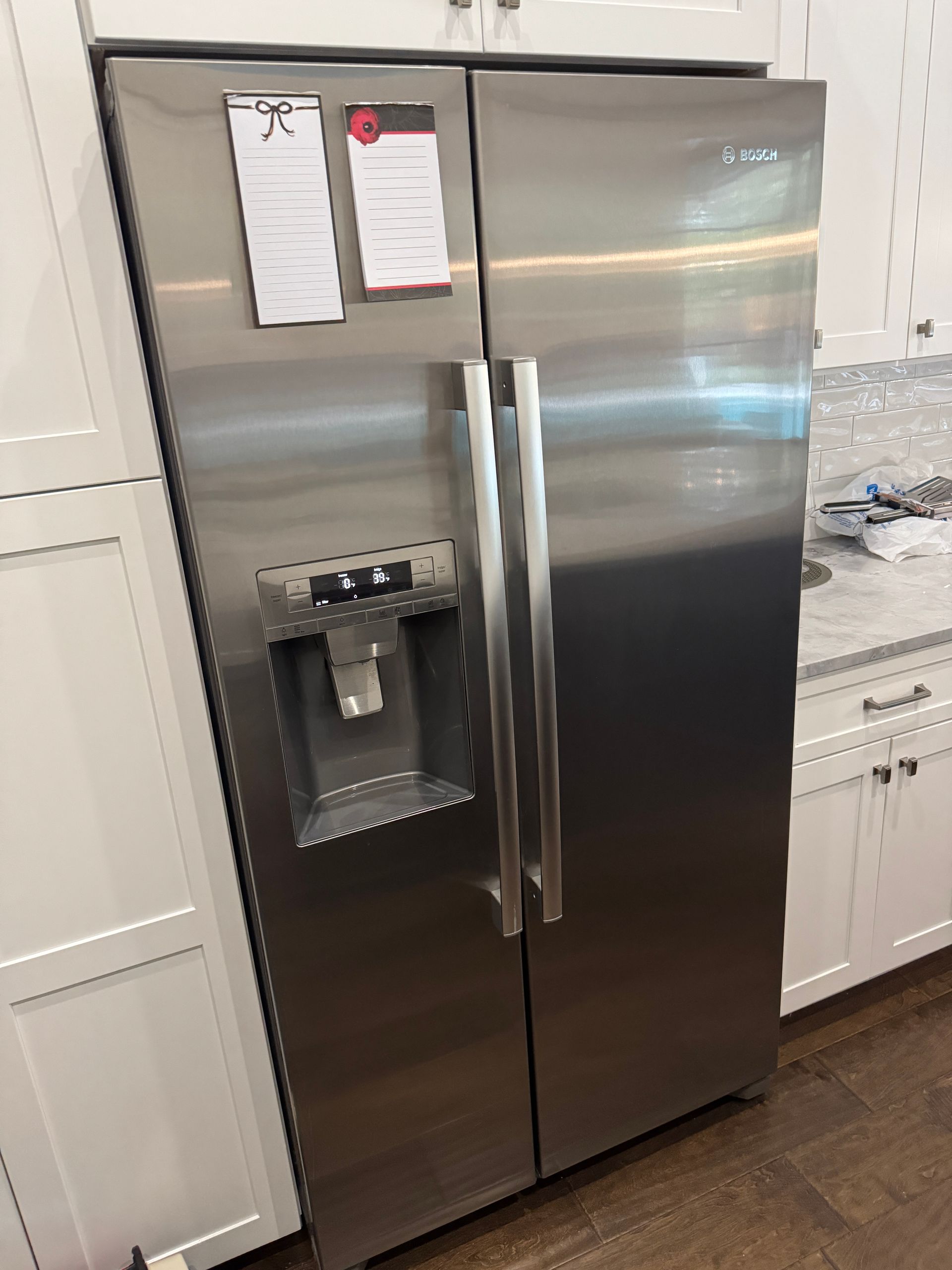 Stainless steel Bosch side-by-side refrigerator in a kitchen with white cabinets.