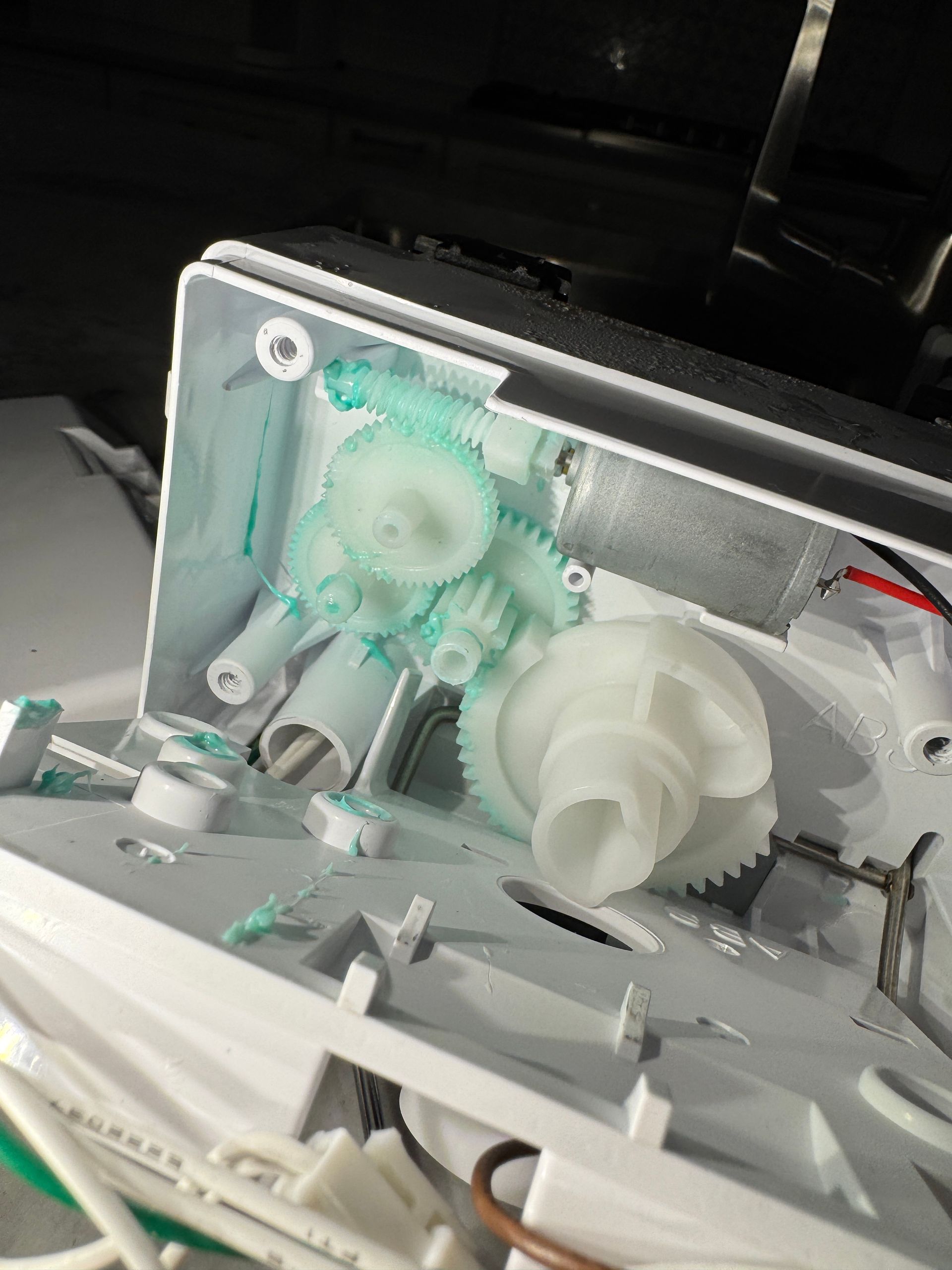 White plastic printer parts with green gears, inside a damaged printer.