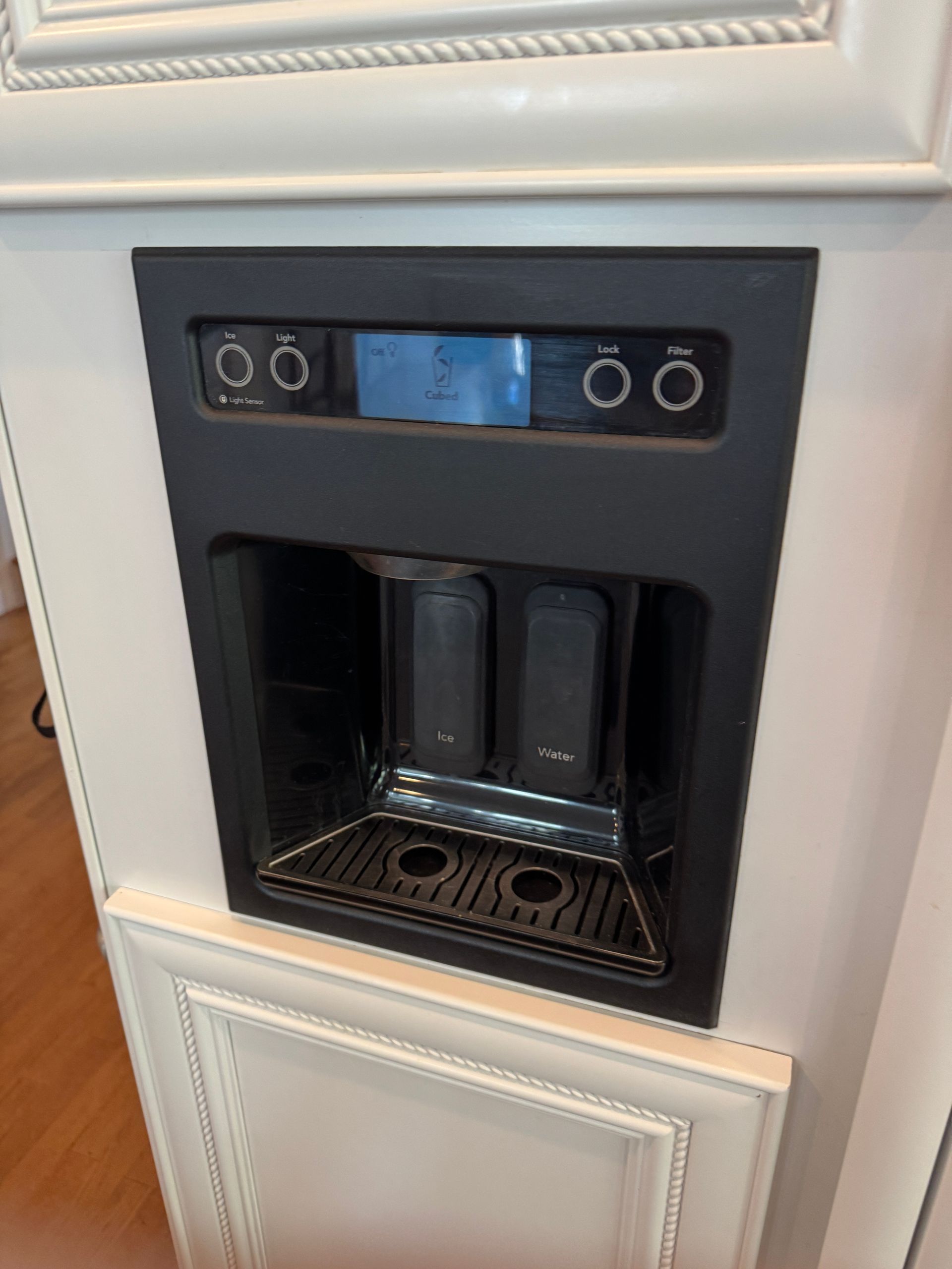 Built-in coffee maker in a white cabinet, with a black control panel and water/cup area.