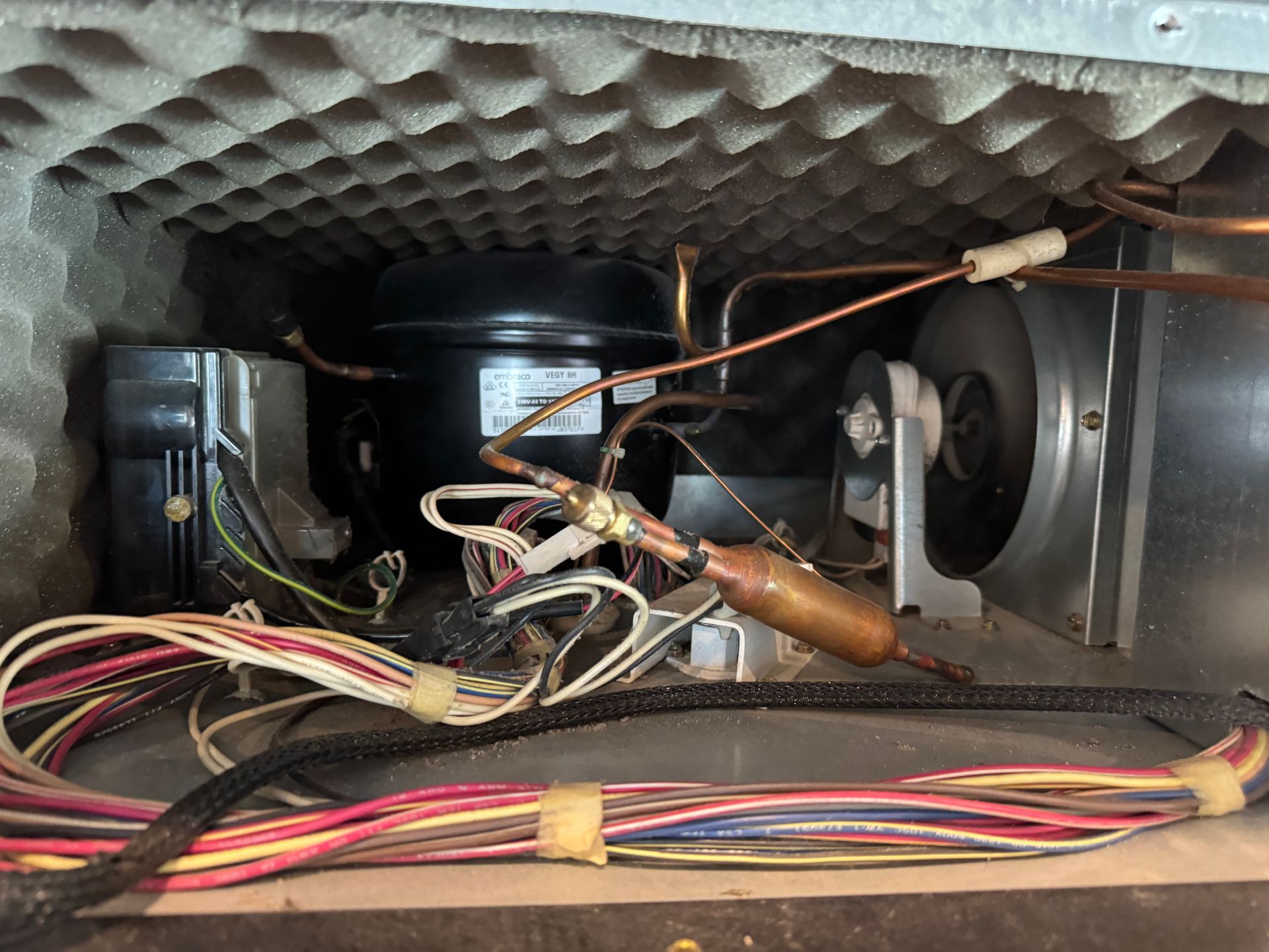A refrigerator compressor and components inside the machine; copper tubes, wiring, and fans are visible.