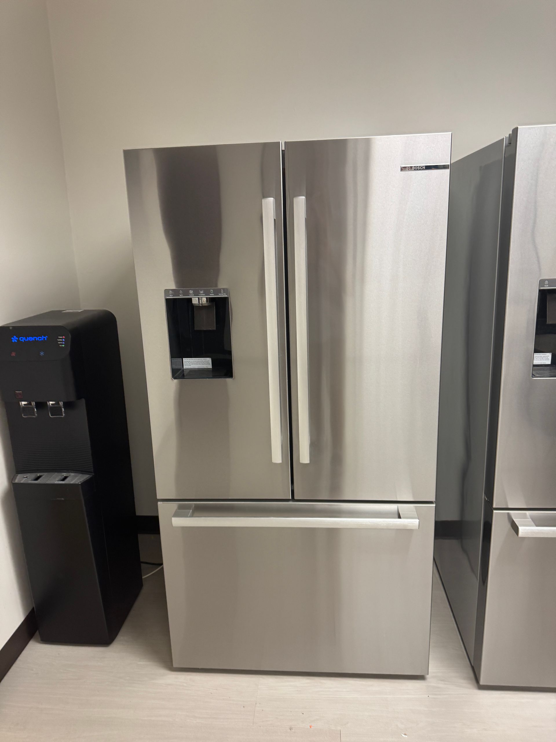 Stainless steel French door refrigerator with water dispenser next to a black water cooler.
