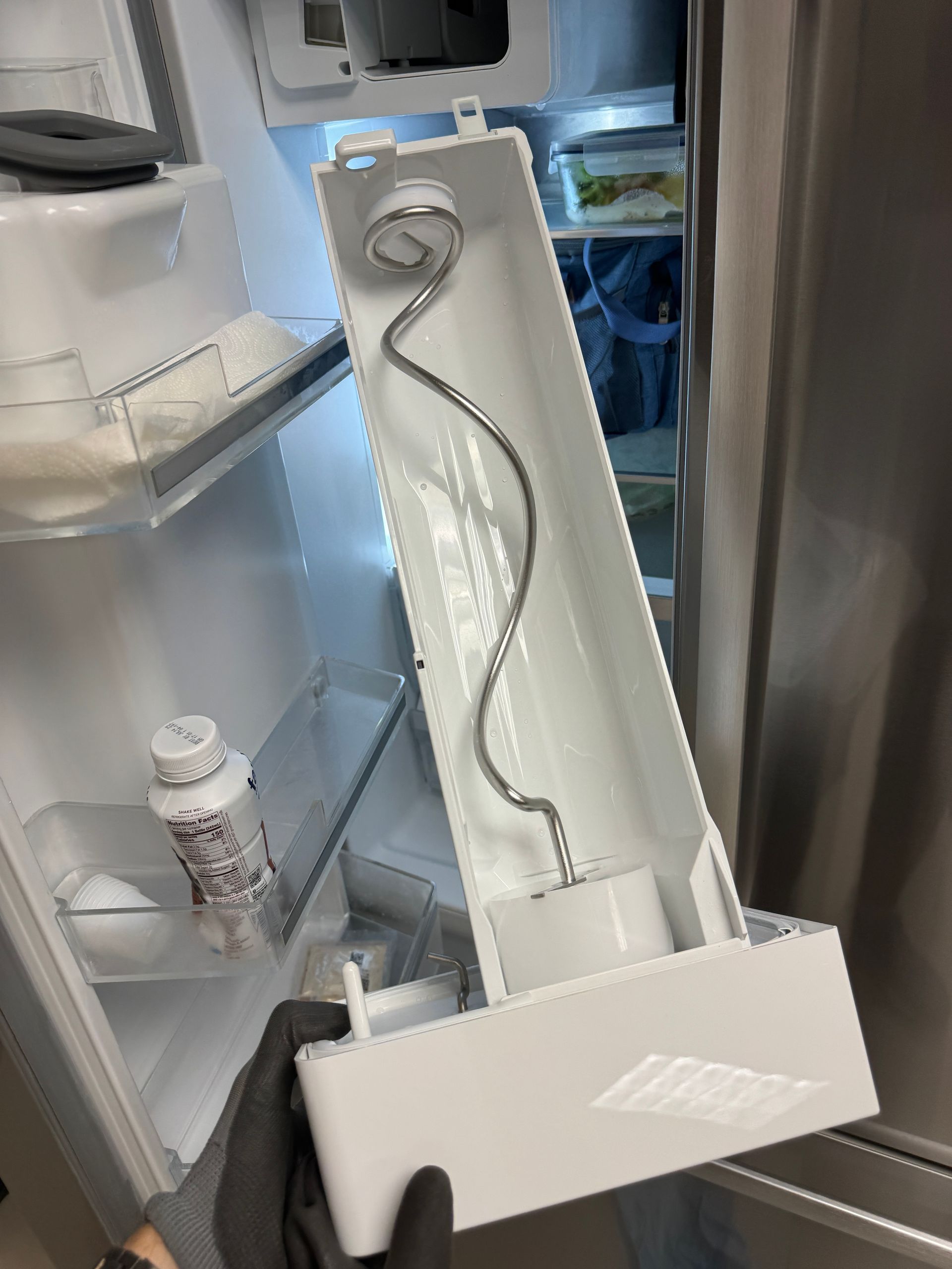 Refrigerator ice maker assembly being removed, revealing the interior of the fridge.