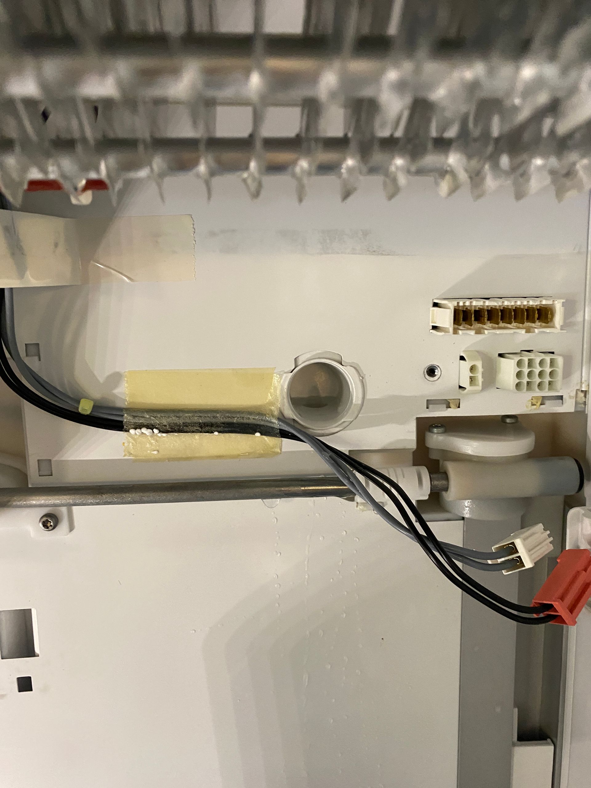 Interior of a refrigerator showing wiring, insulation tape, and plastic components, likely for a water or ice dispenser.