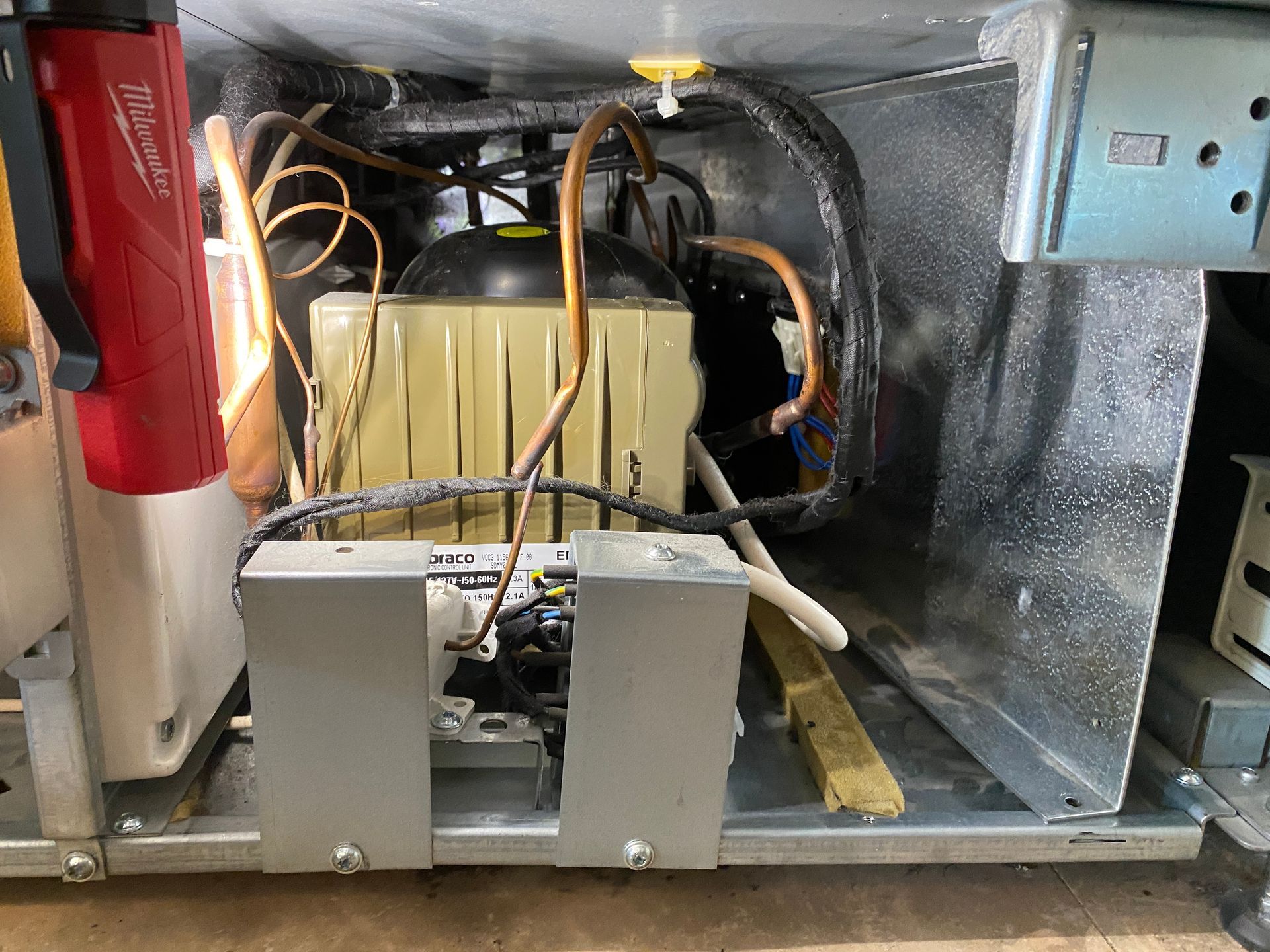 Inside view of a refrigeration unit with copper tubing, a compressor, and electrical components.
