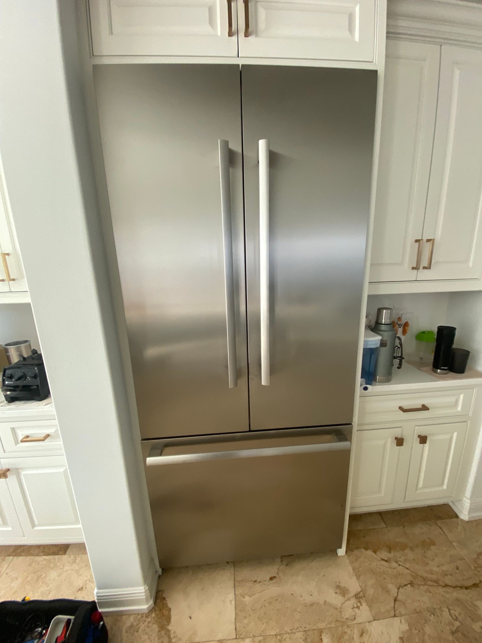 Stainless steel French-door refrigerator built into white cabinetry in a kitchen.