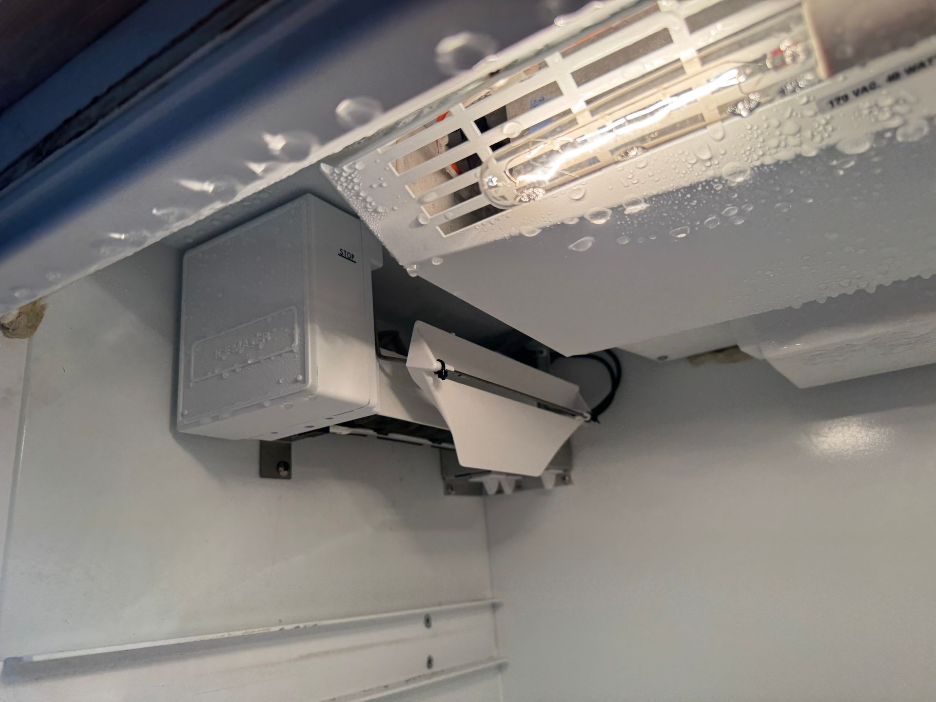 Interior of a refrigerator with an ice maker, covered in frost.