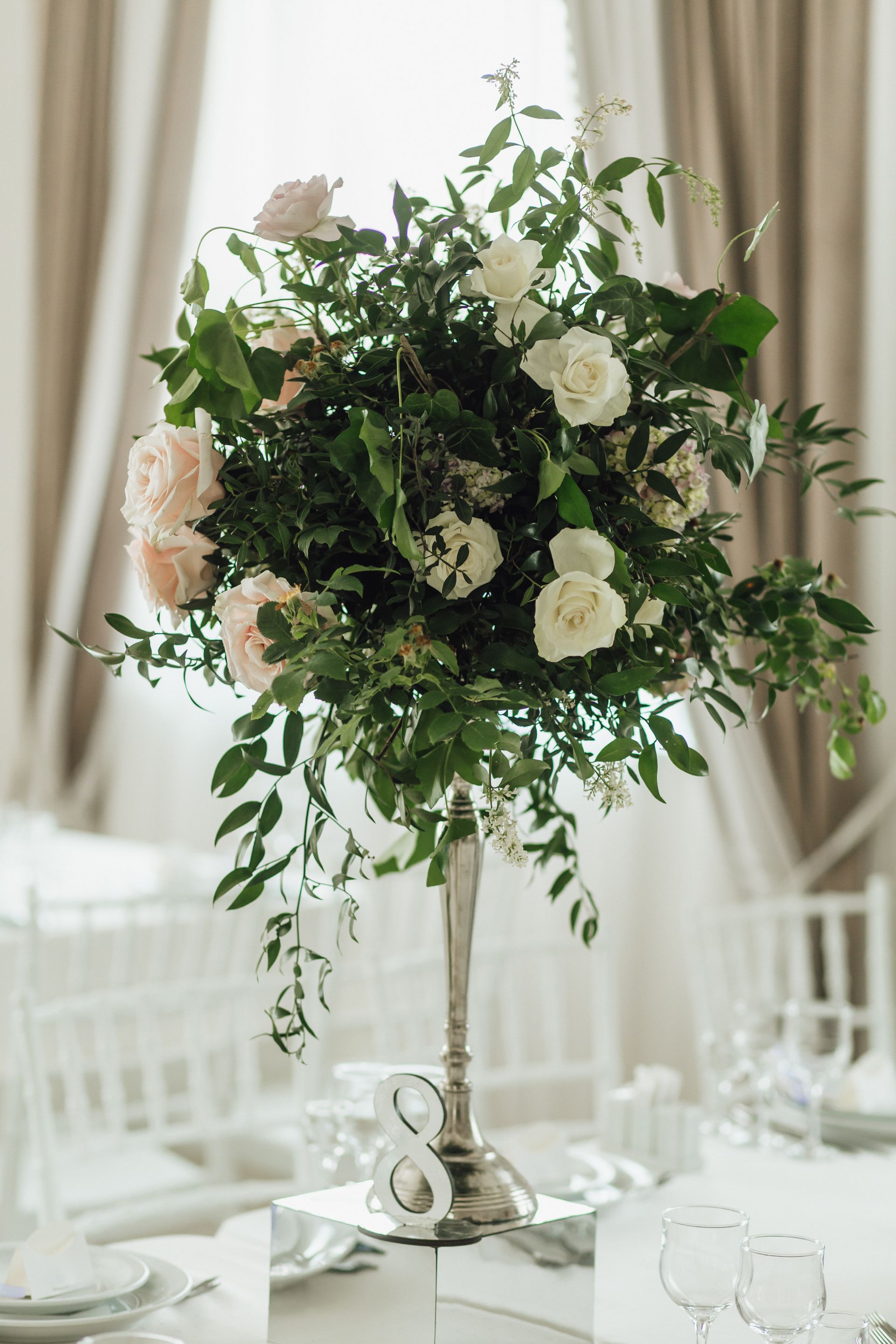 A tall vase filled with flowers and greenery is on a table.