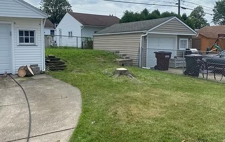 Backyard with concrete patio, grassy slope, detached garage, and white house under a cloudy sky