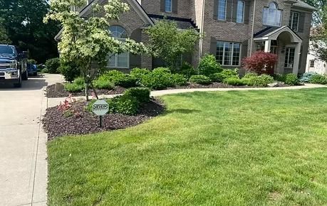 Suburban house with stone facade, landscaped front yard, driveway, and manicured green lawn.