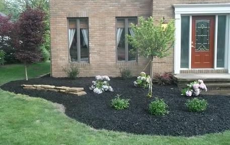 Brick house front yard with black mulch, small shrubs, flowers, and a red front door