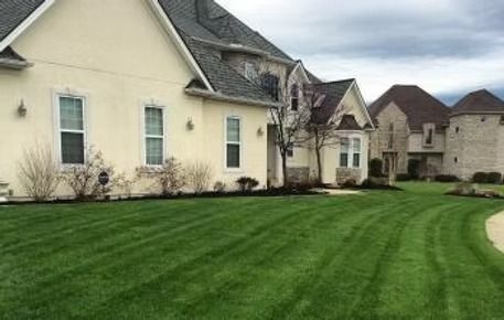 Suburban homes beside a neatly mowed green lawn under a cloudy sky