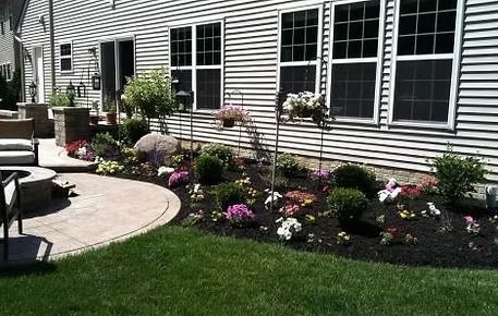 Landscaped garden beds with pink and white flowers beside a house and patio
