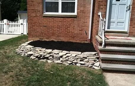Brick house exterior with stone landscaping bed and front steps beside a white door