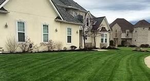 Suburban houses with beige siding and a neatly striped green lawn along a curved driveway