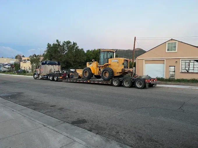 A yellow tractor is on a trailer on the side of the road