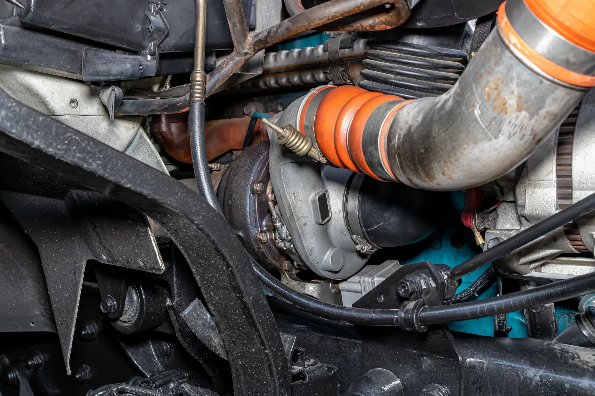 A close-up view of a vehicle engine bay, focusing on the metallic turbocharger and its connected orange rubber hose.