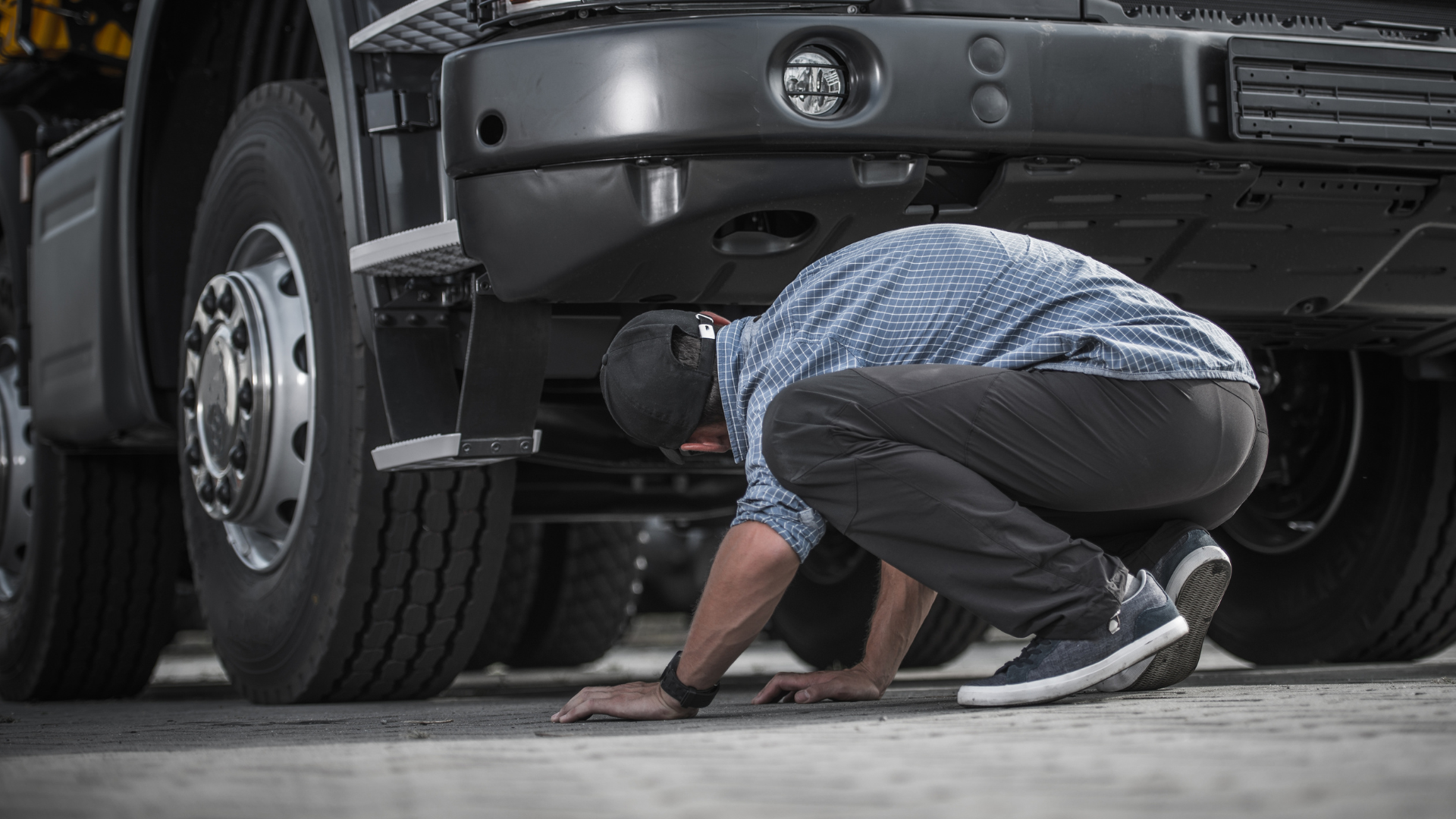 A man is kneeling down under the hood of a truck.