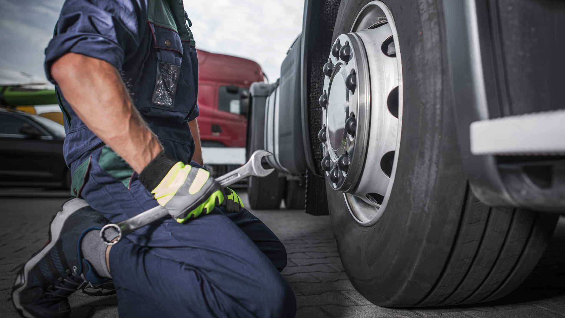 A man is kneeling down to fix a truck tire with a wrench.