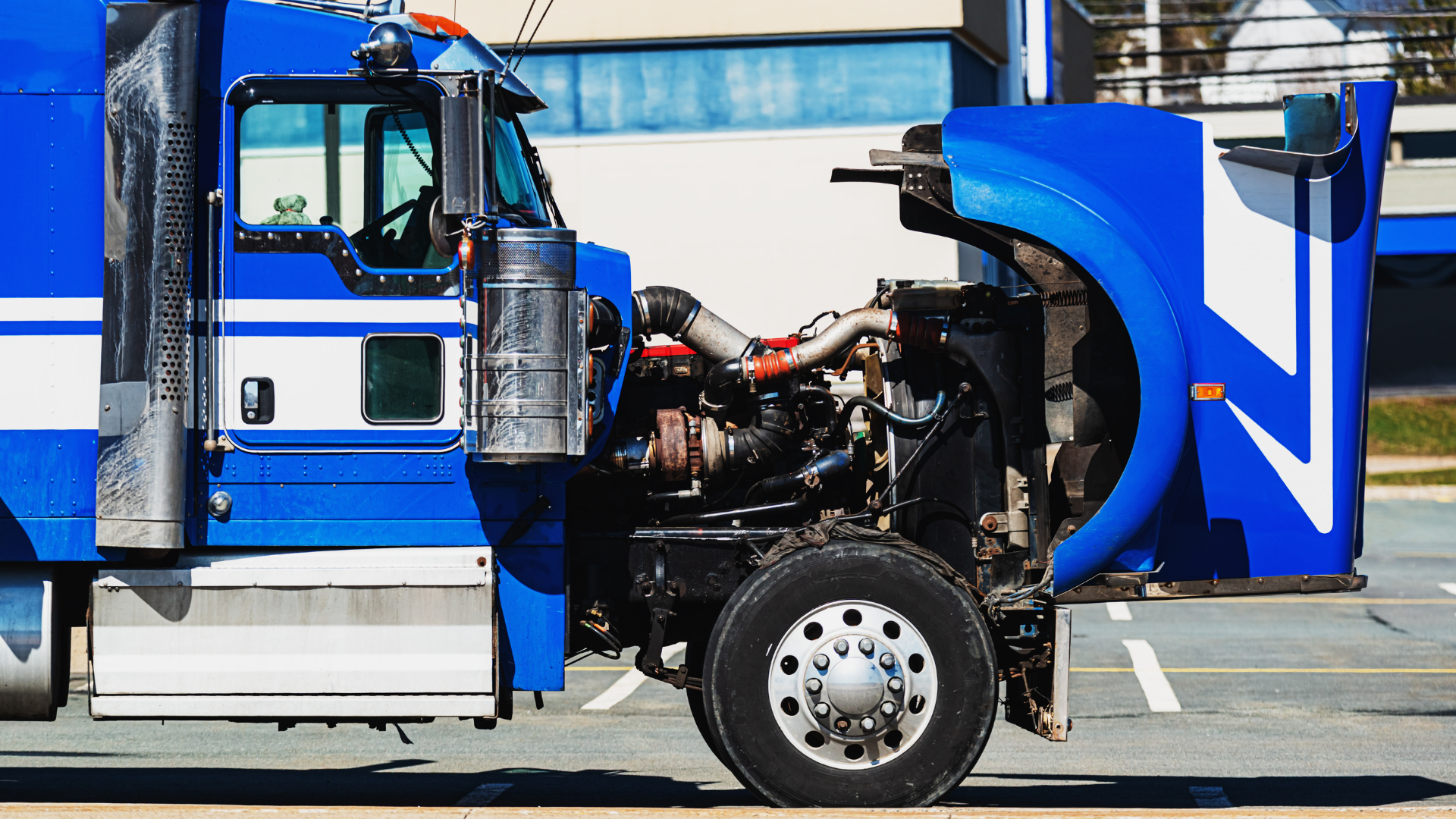 A blue semi truck with its hood open is parked on the side of the road.