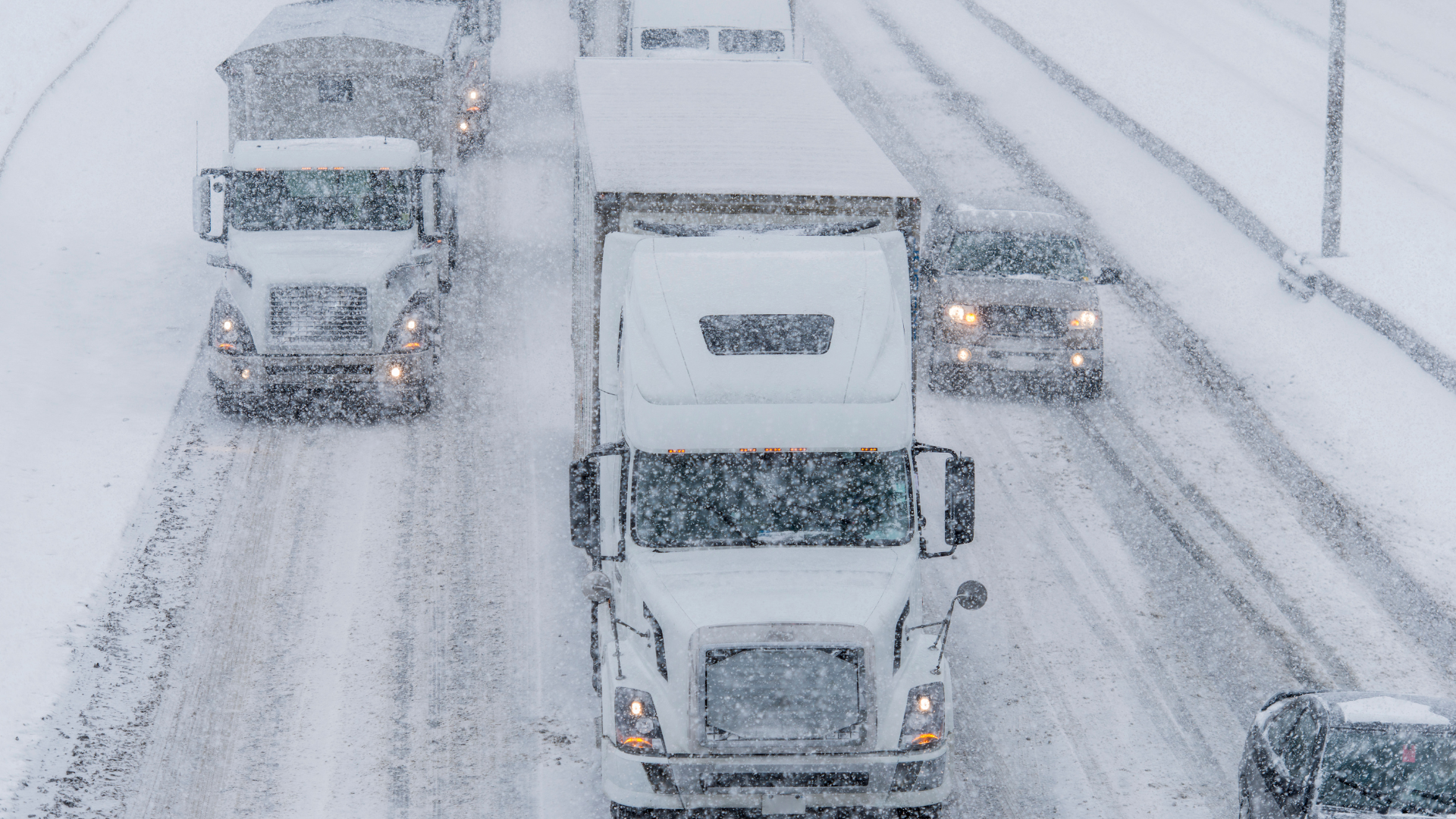 A row of trucks are driving down a snowy highway.