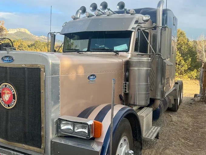 A semi truck is parked in a dirt field with mountains in the background.