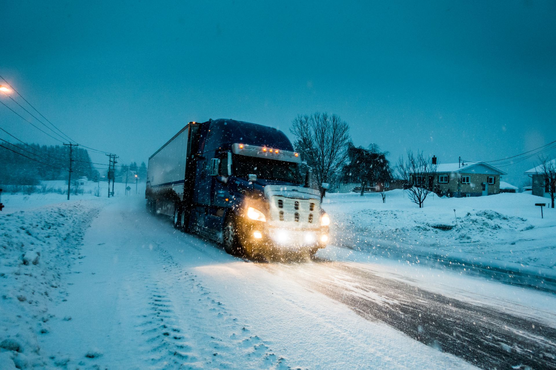 Semi-truck driving on a snow-covered road at night, headlights on.