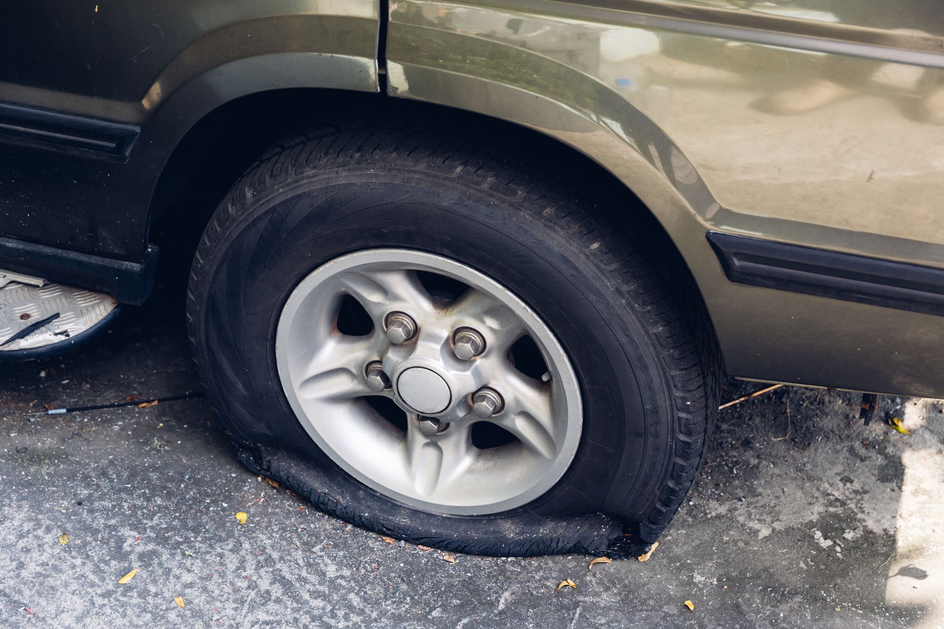 Flat tire on a green vehicle with a silver wheel, parked on pavement.