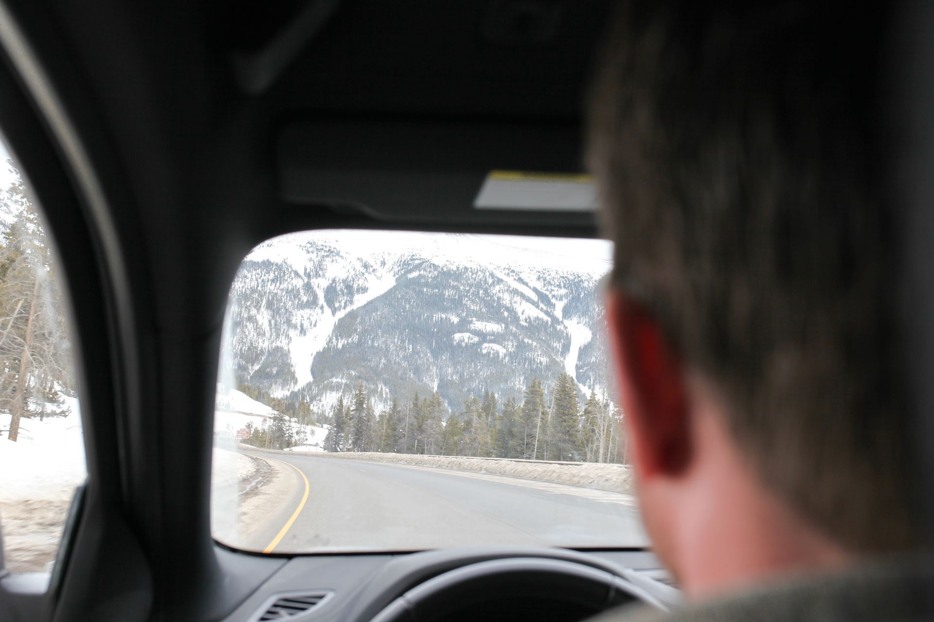 Person driving a car, looking at a snowy mountain scene through the windshield.