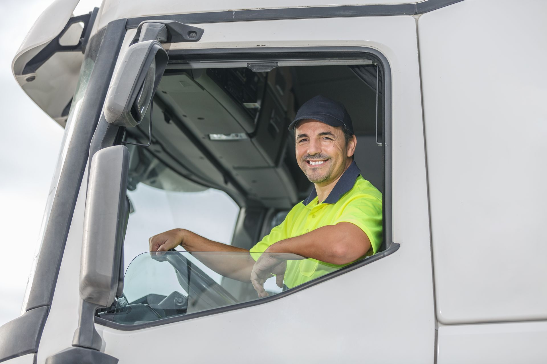 Truck driver smiling in his cab. Wearing a cap and bright yellow shirt.
