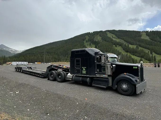 A semi truck is parked on the side of the road with mountains in the background.