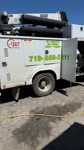 A white utility truck with the doors open is parked on the side of the road.