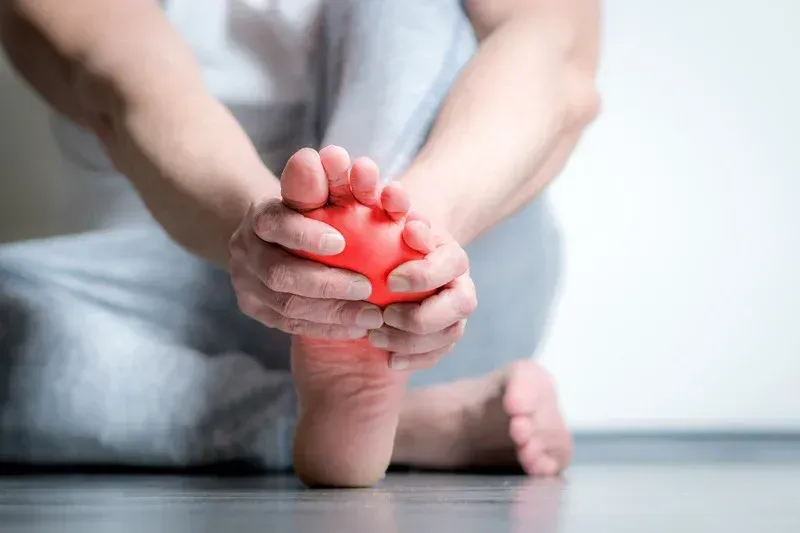 A person is sitting on the floor holding a red ball to their foot.