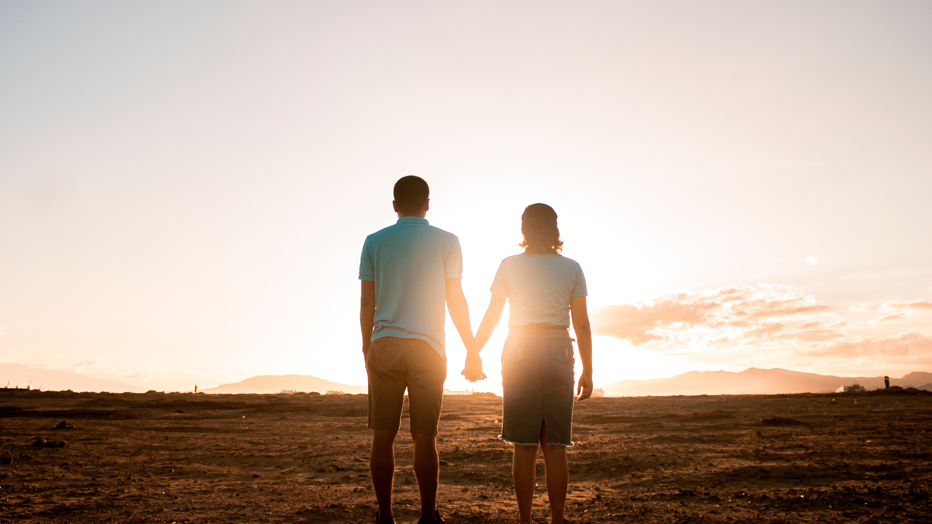 A man and a woman are holding hands while standing in a field at sunset.