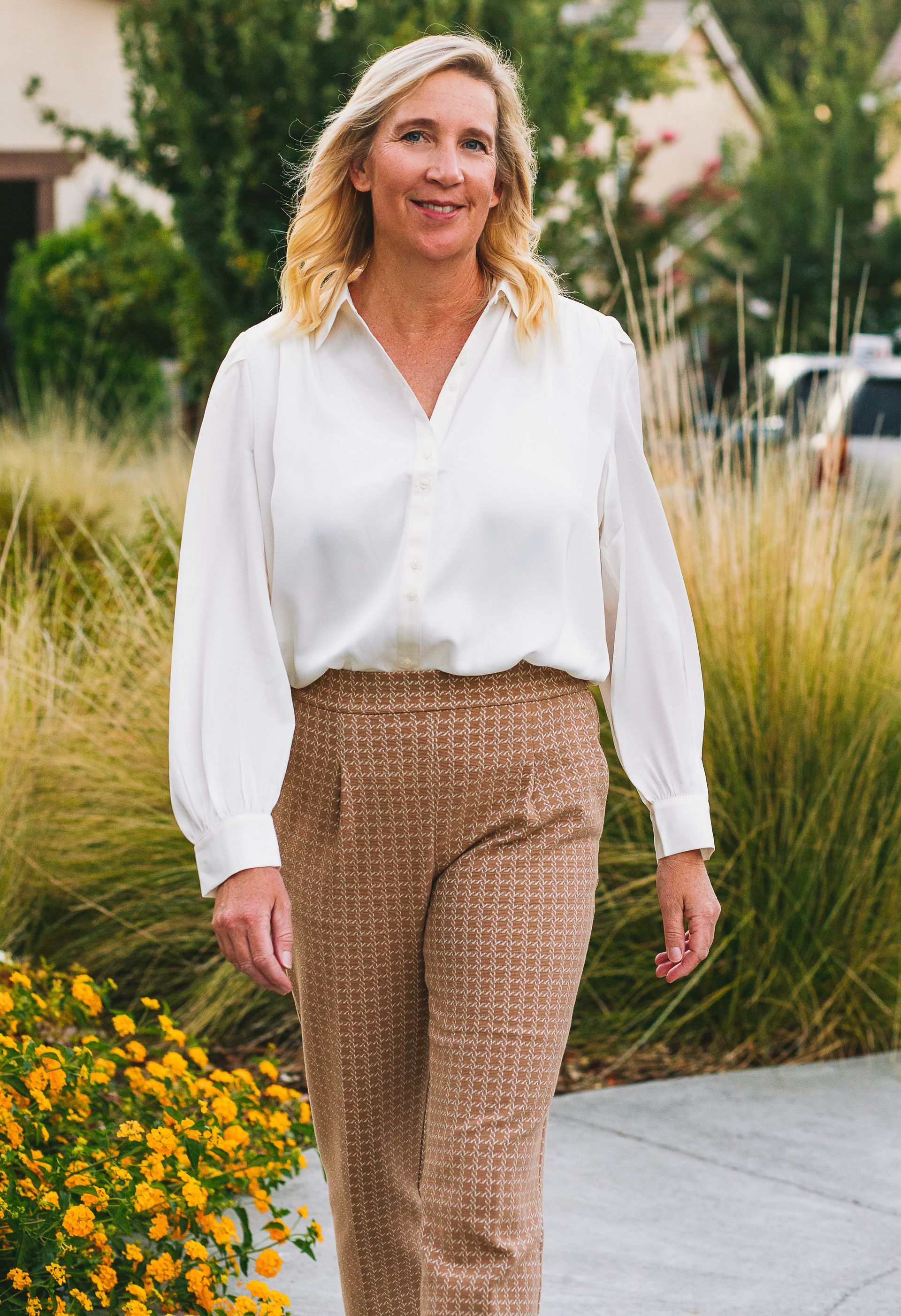 A woman in a white shirt and brown pants is walking down a sidewalk.