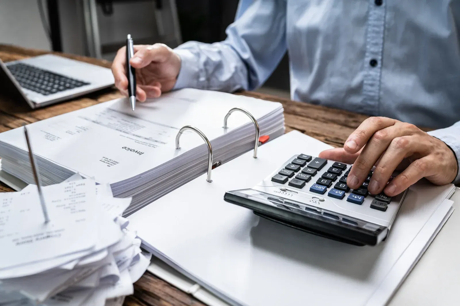 Person calculating finances with calculator, pen, and paperwork at a desk.