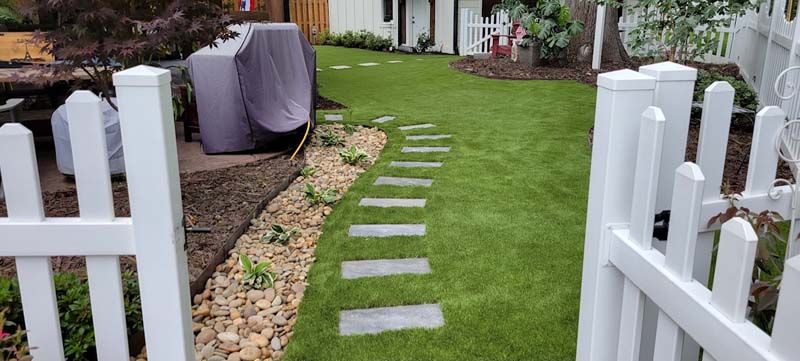 A white picket fence surrounds a lush green lawn in a backyard.