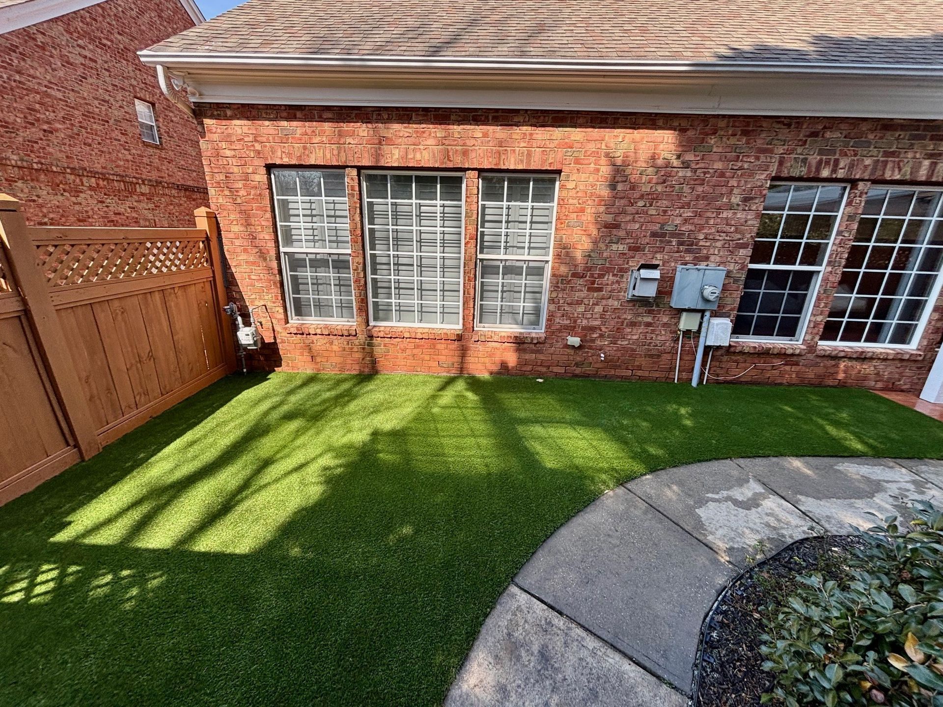 A brick building with three windows, a patch of green turf, and a stone walkway.