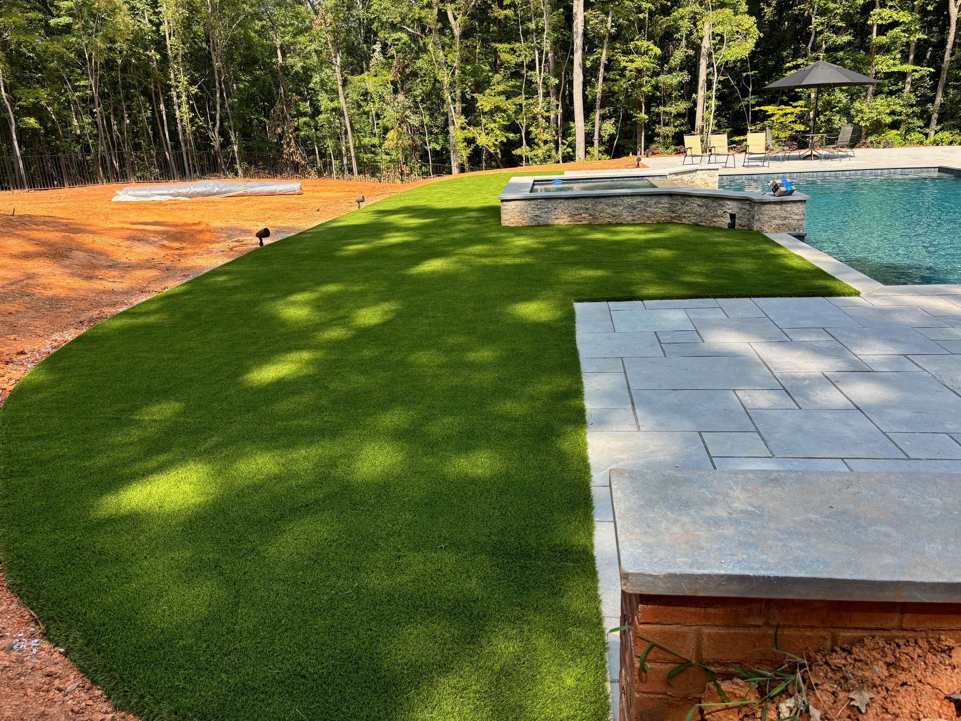 A lush green lawn next to a swimming pool in a backyard.