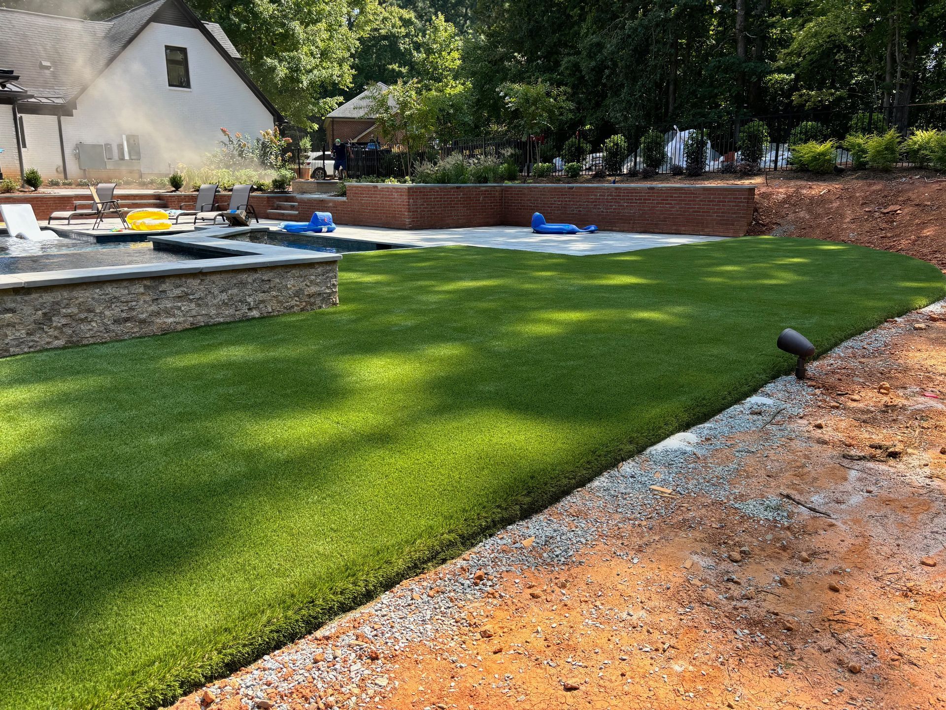 A lush green lawn with a brick wall and a swimming pool in the background.