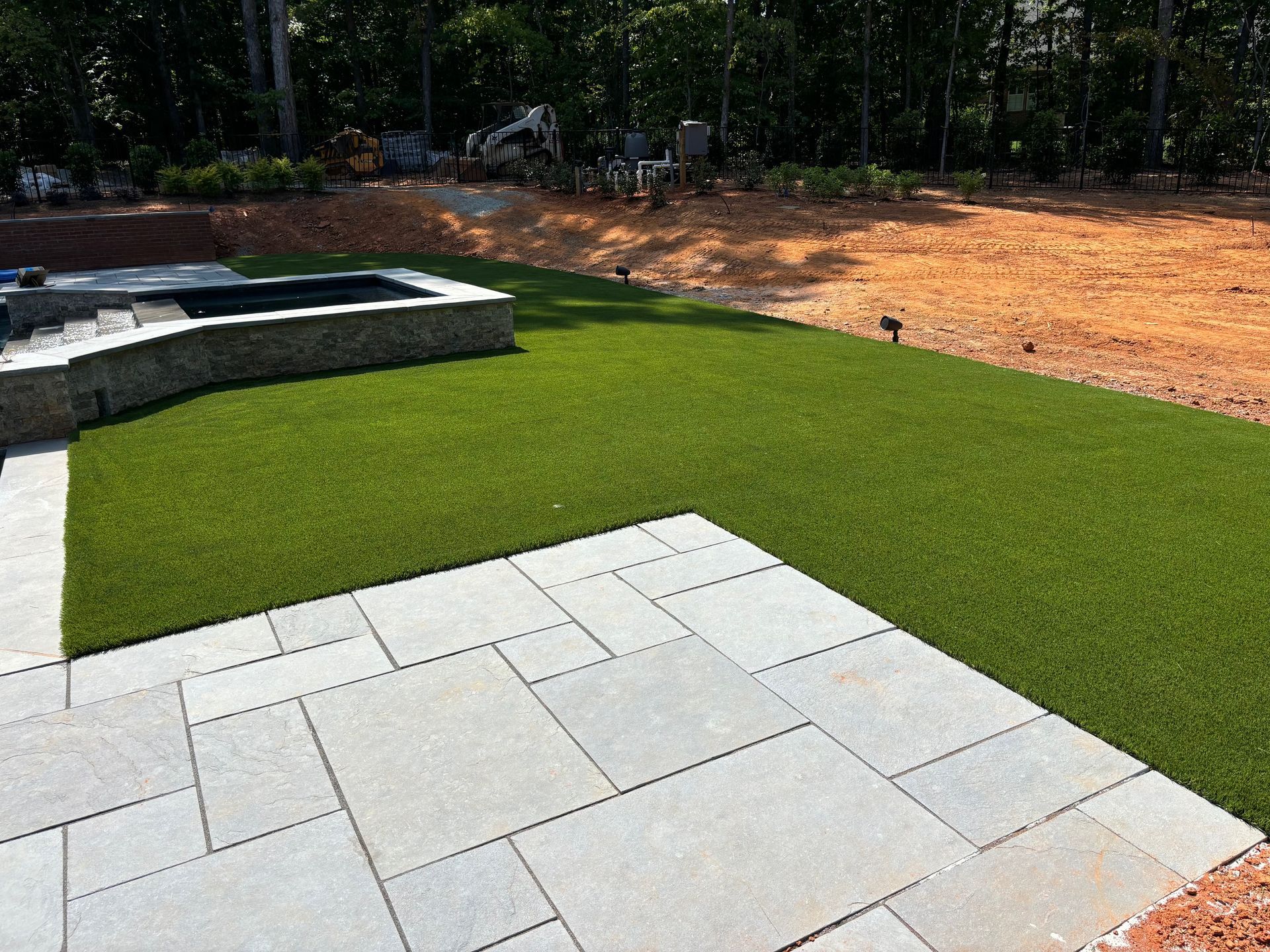 A lawn with a patio and a pool in the background.
